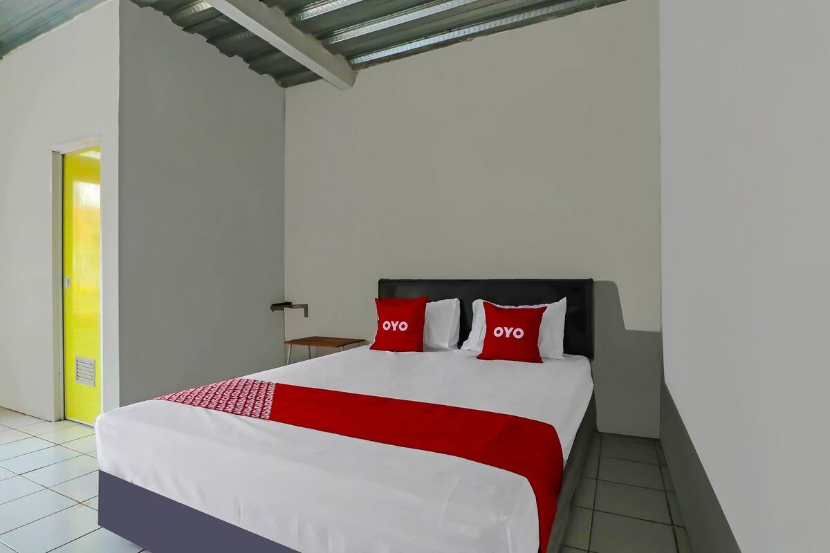 Una habitació d'hotel amb un llit, una tauleta de nit i una porta que condueix a una altra habitació.