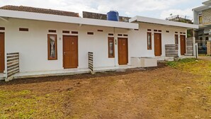 Una hilera de edificios blancos con números en las puertas, un tanque de agua azul en el techo, y un suelo de tierra con poca hierba.