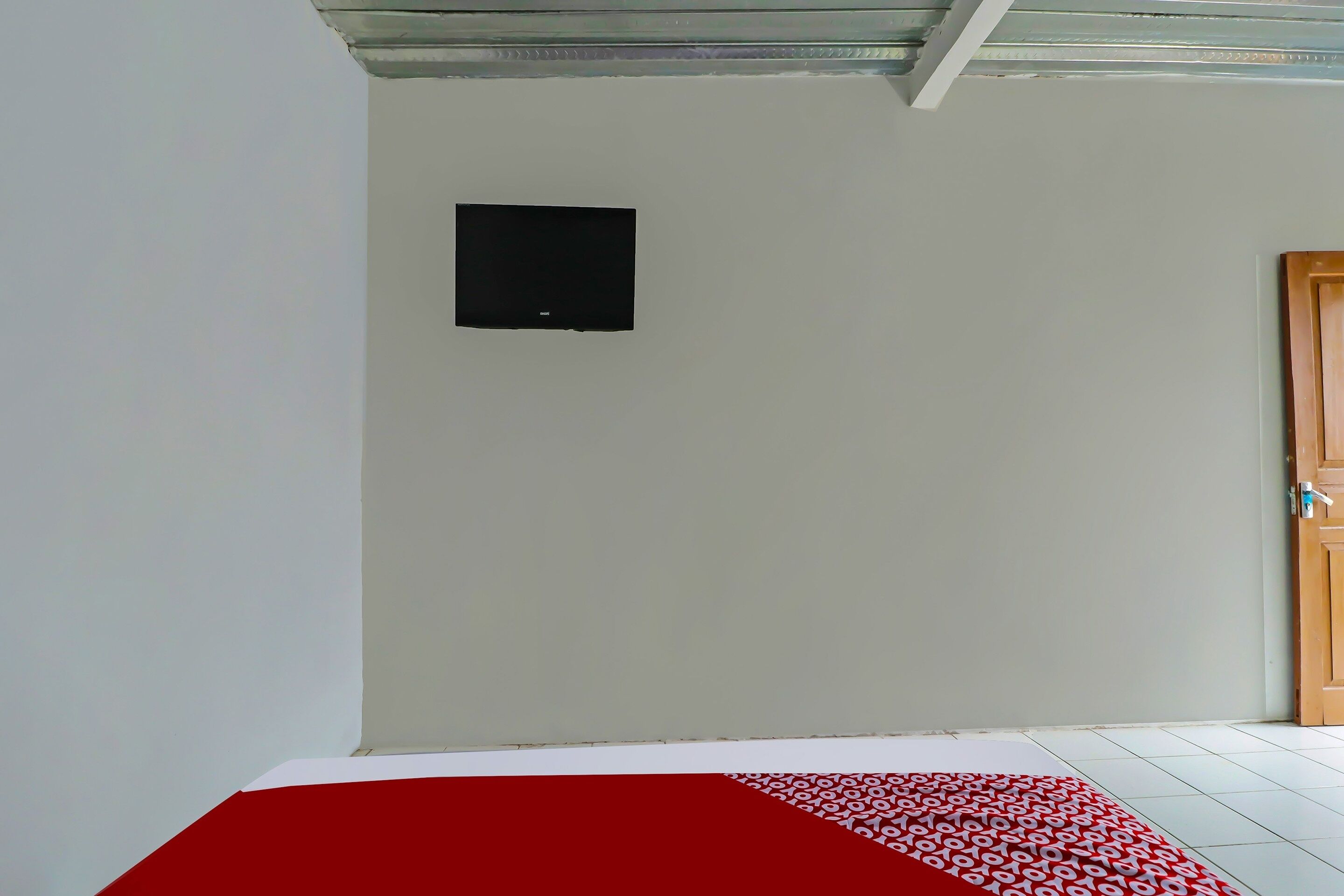 A room with a tiled floor, a red patterned rug, a wooden door, and a black framed object on the wall.