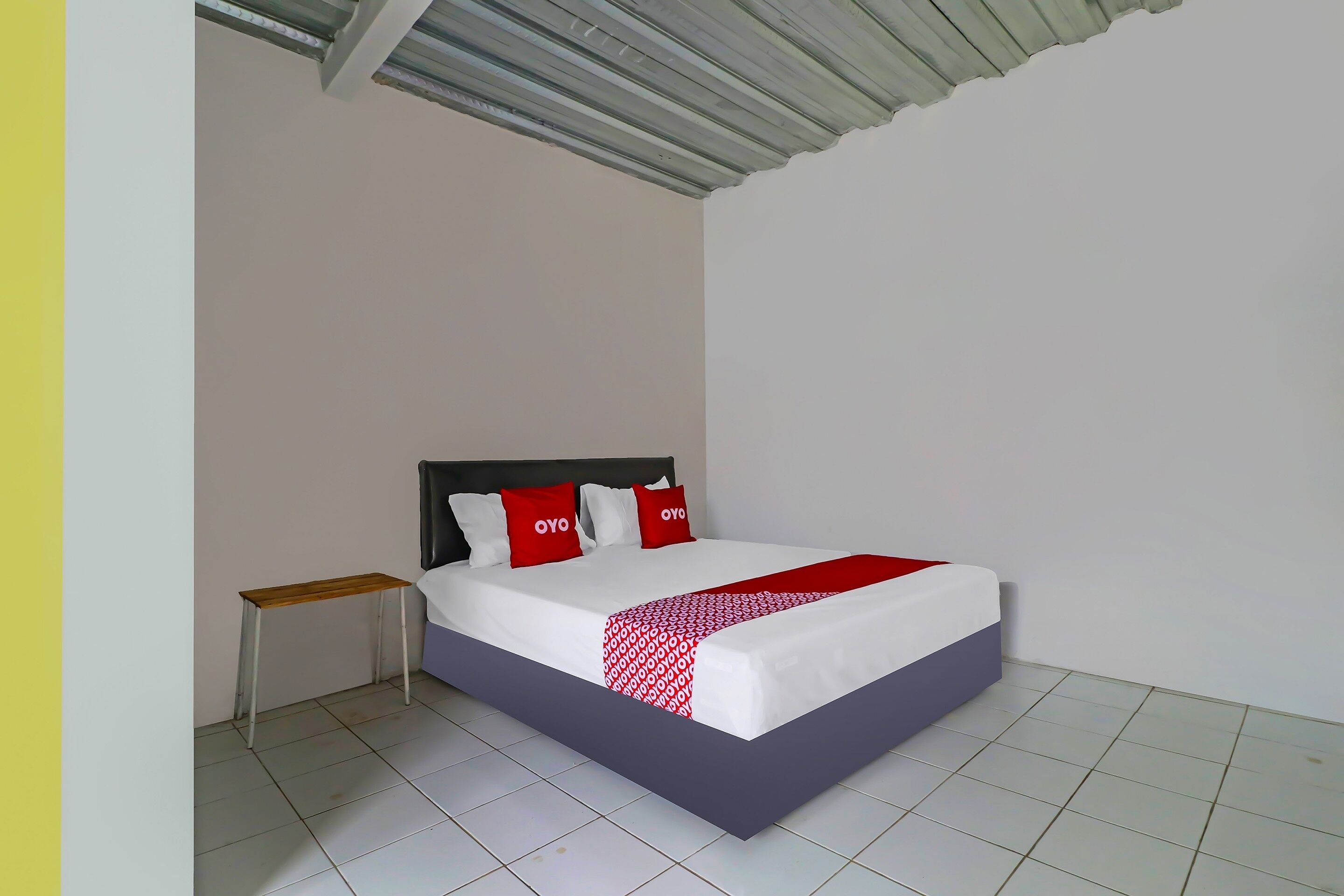 A neatly made bed with a red and white bedspread, a wooden nightstand, and a headboard with two red pillows.