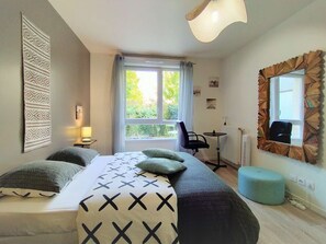 Un dormitorio con cama, escritorio, silla, ventana con cortinas y espejo con marco decorativo.