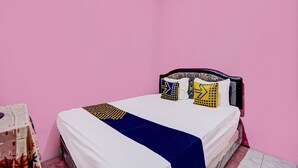 A bedroom with a bed against a pink wall, featuring a white mattress, a blue bedspread, and patterned pillows. - Hotel O Nurul Homestay Syariah (Gresik)