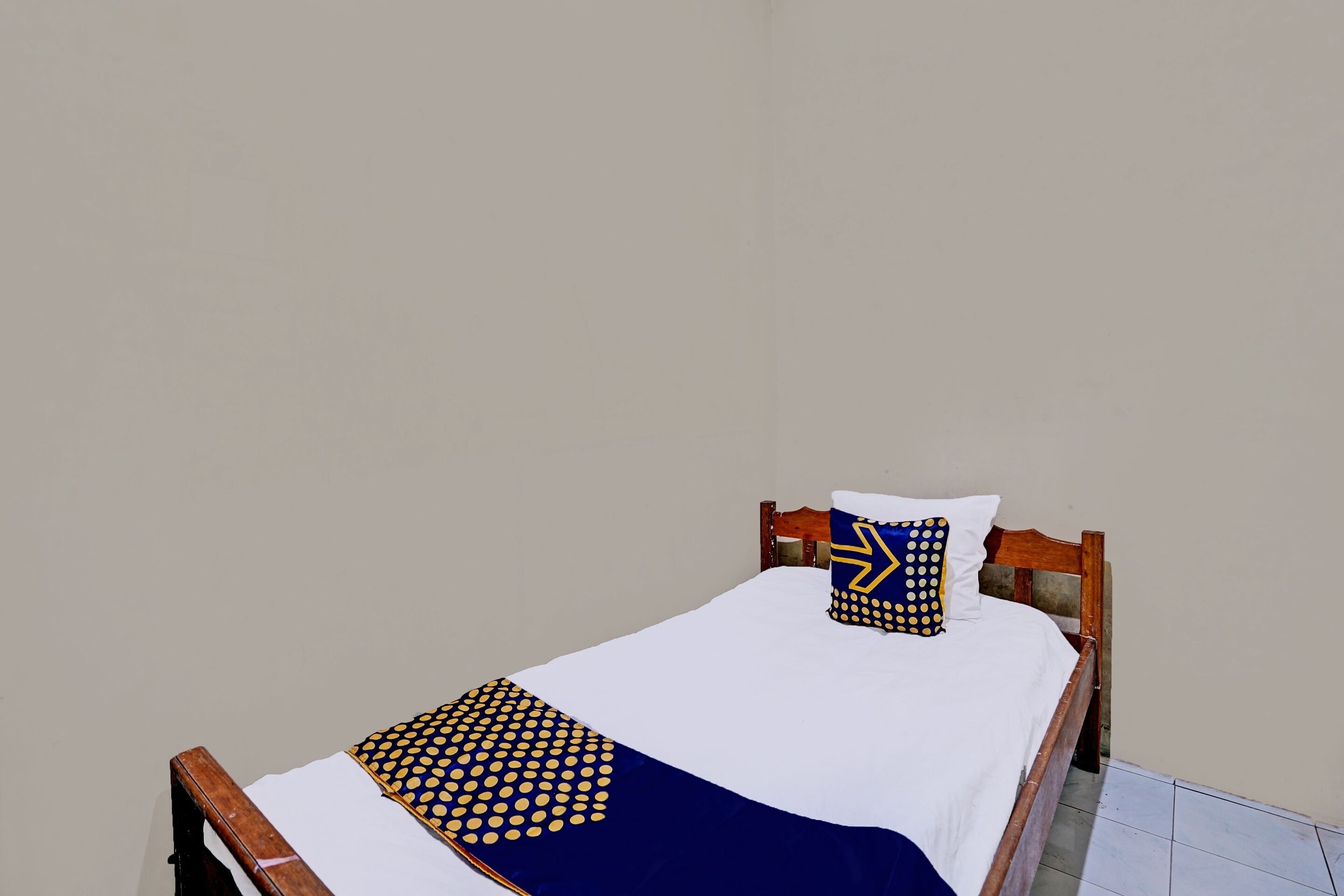 Una cama individual con estructura de madera, ropa de cama blanca y una colcha de lunares azules y amarillos.