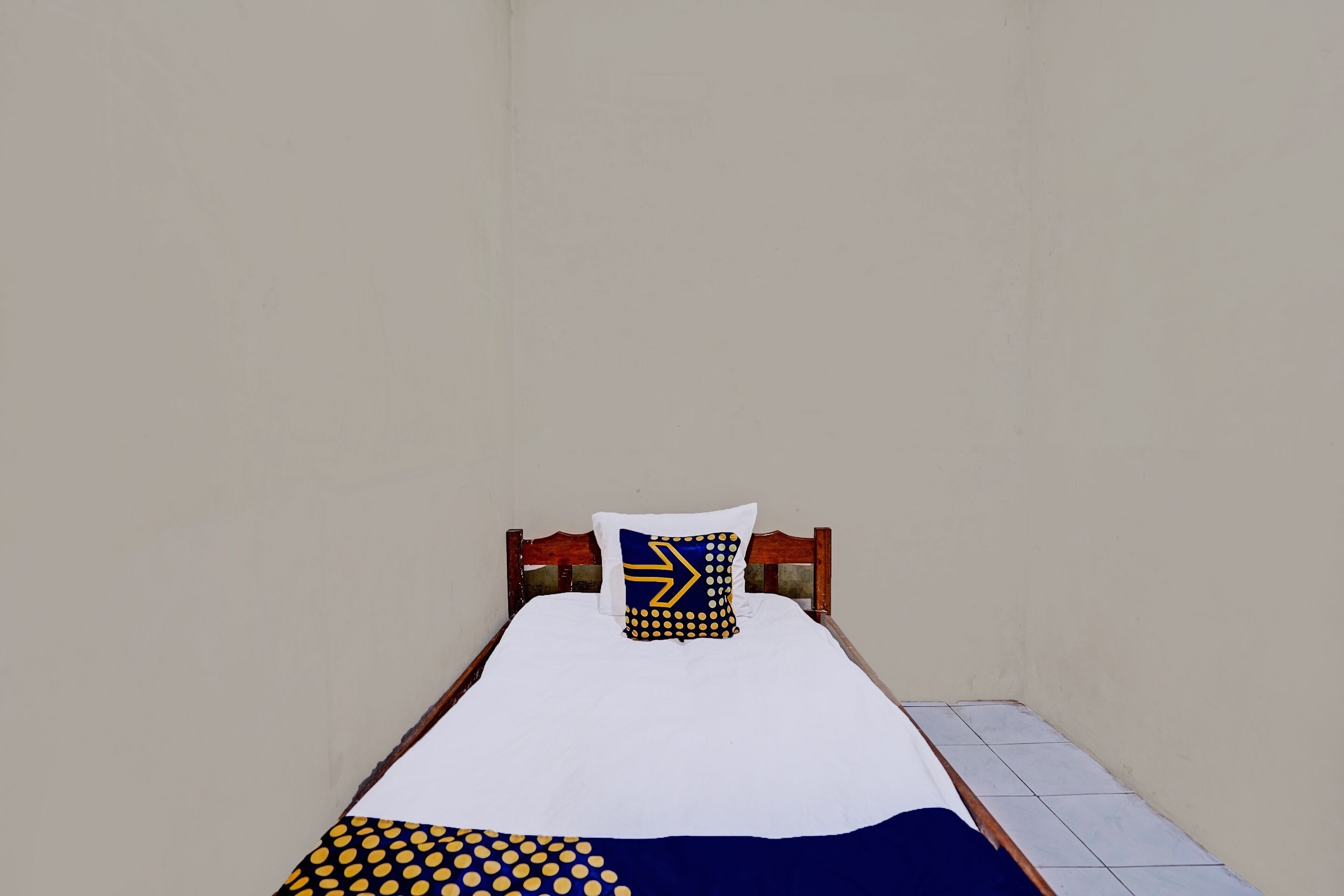 Een eenpersoonsbed met een witte matras, een blauwgeel kussen en een blauwgeel dekbed.