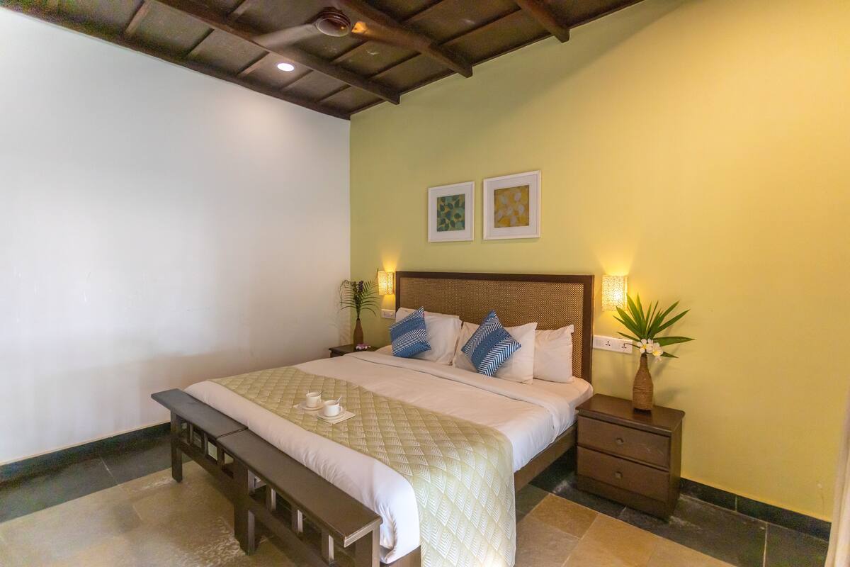 Un dormitorio ordenado con cama, mesitas de noche, un banco y decoración en la pared.
