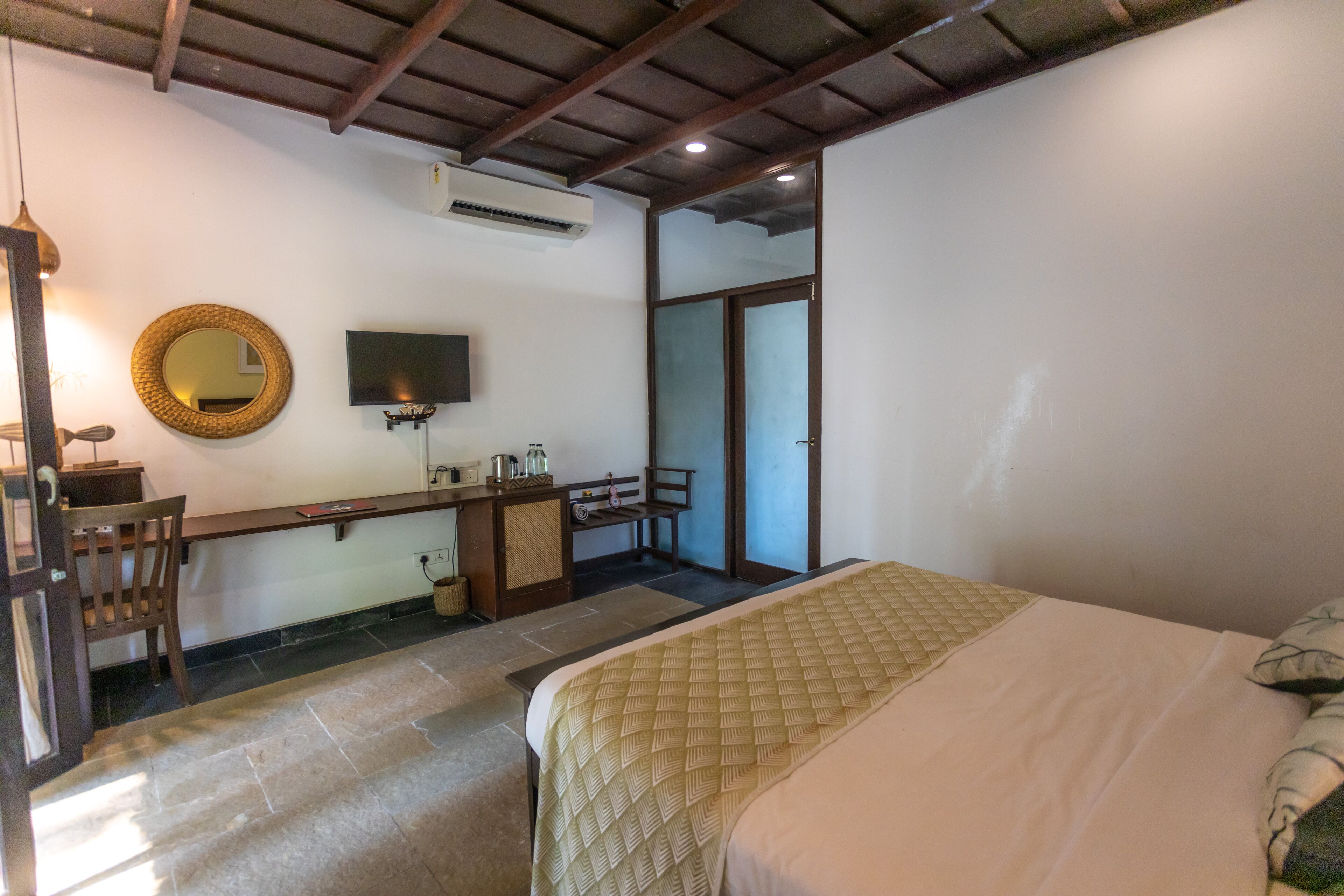 Quarto de hotel com cama, escrivaninha com cadeira, televisão, espelho e porta de correr que dá para uma varanda.