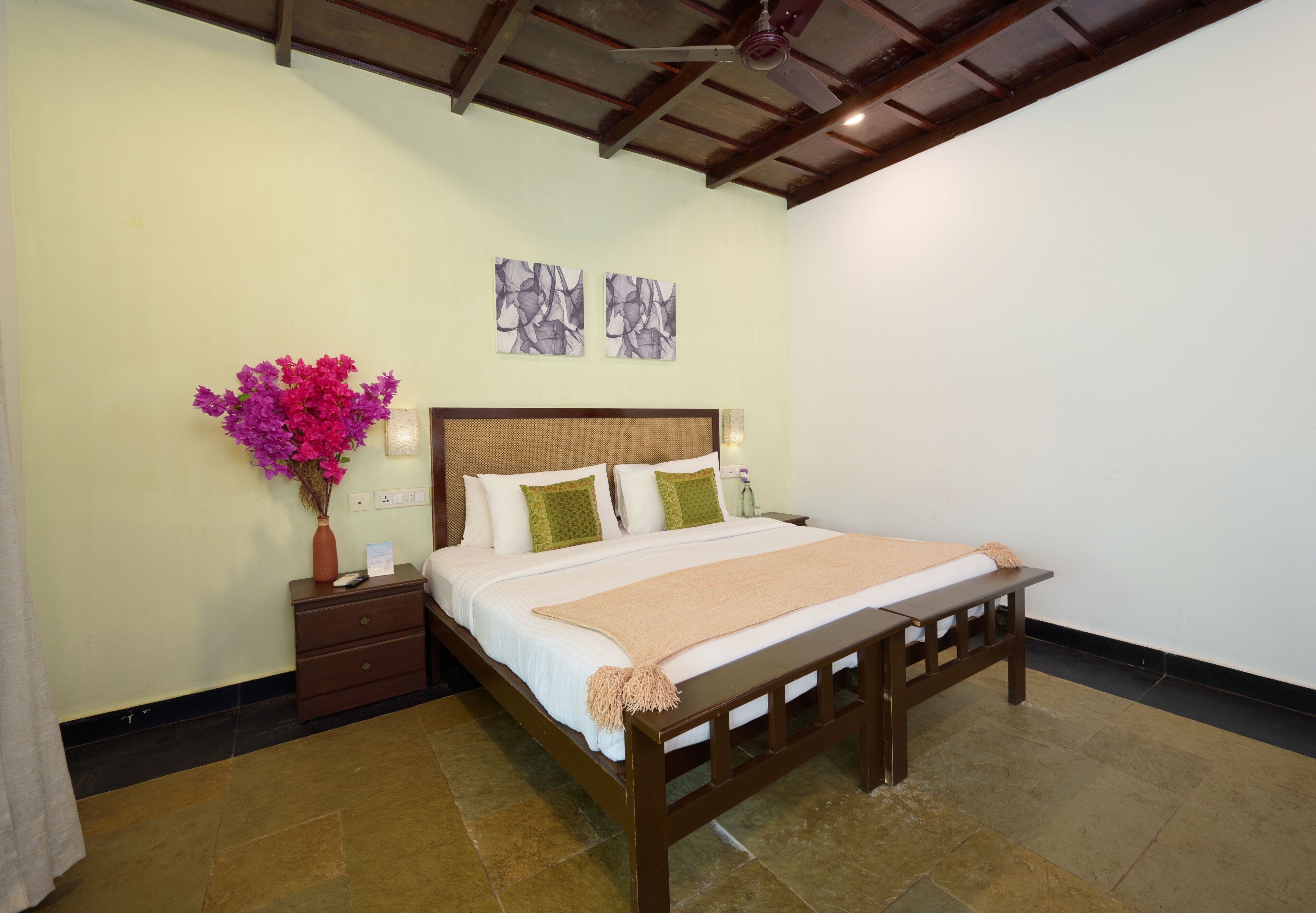 A bedroom with a wooden bed, a nightstand, a vase with flowers, and two wall art pieces.