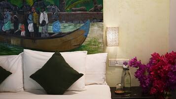 A bed with white bedding and green pillows, a nightstand with a bottle and glass, a wall-mounted light, and a painting of a boat scene.