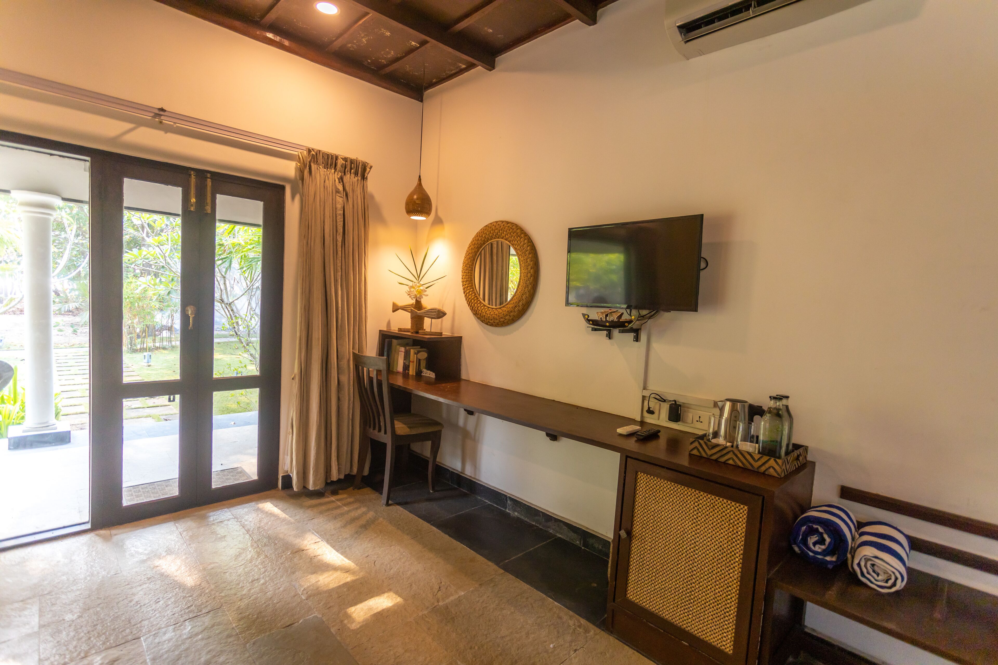 A room with a desk, chair, TV, and a view of greenery outside.