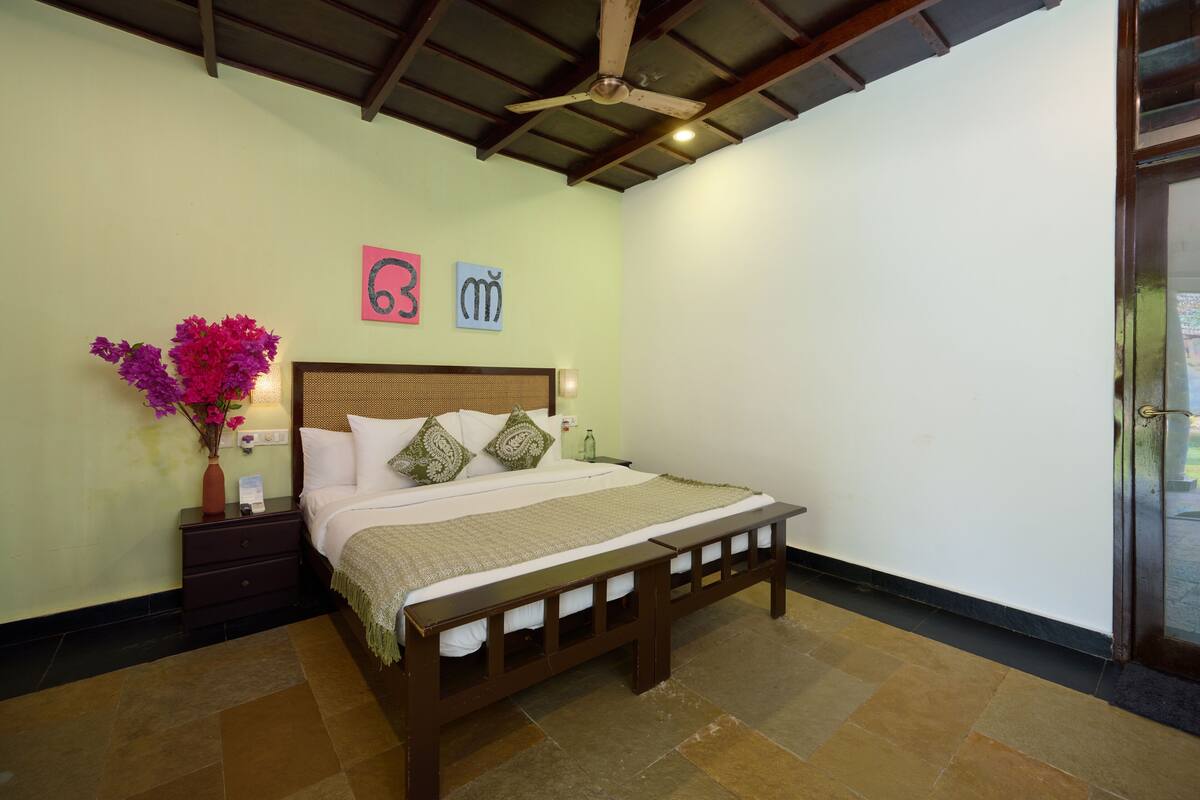 Un dormitorio con cama, mesita de noche y un jarrón de flores.