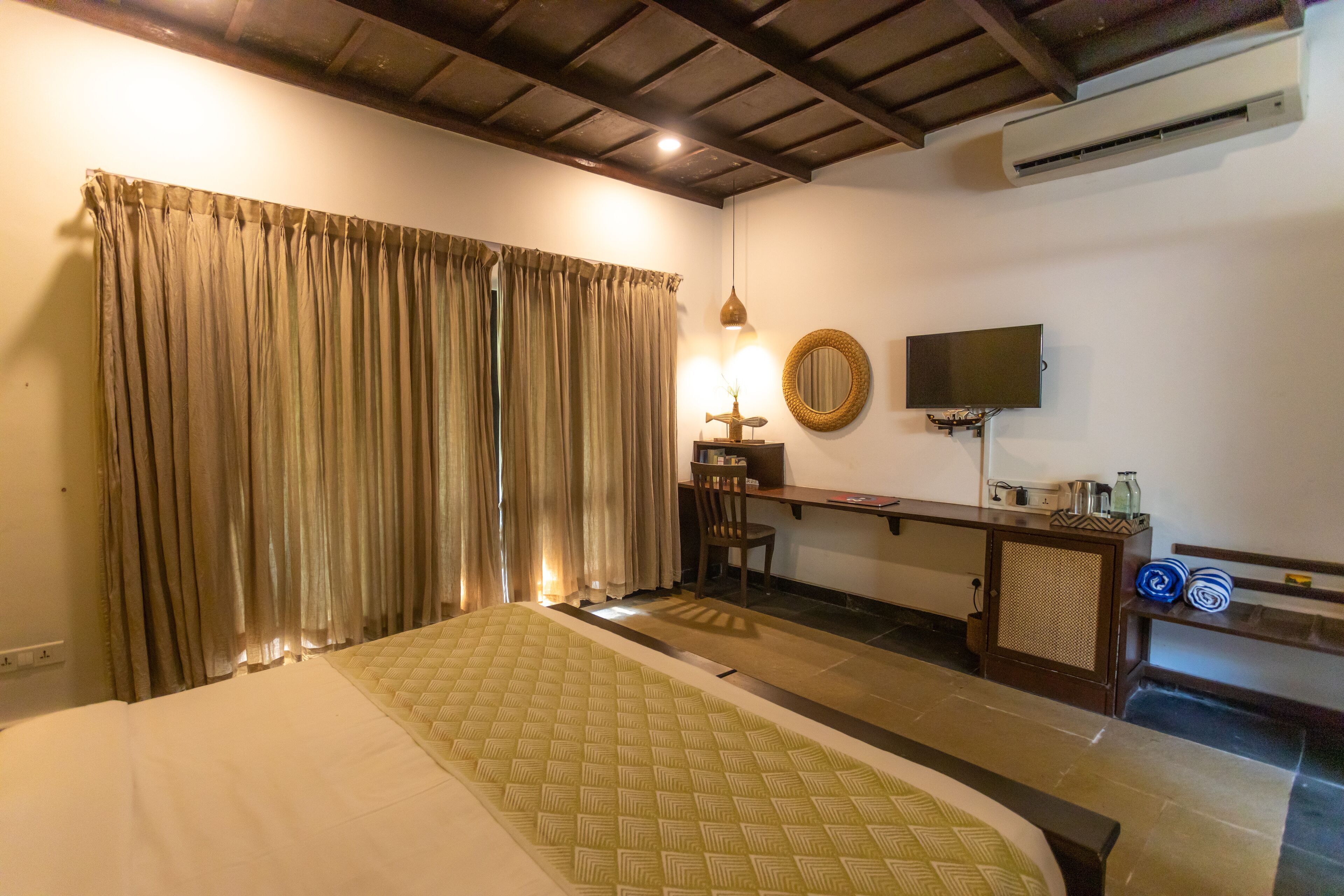 A hotel room with a bed, curtains, a desk with a chair, a television, and a small cabinet.