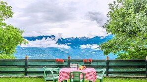 An outdoor dining area with a checkered tablecloth, green chairs, and a view of mountains. - Casa Rita by Interhome (Valtellina)