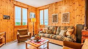 A cozy living room with wooden walls, a patterned sofa, a wooden coffee table, and a lamp. - Casa Rita by Interhome (Valtellina)