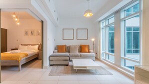 A modern, well-lit room with a bed, a sofa, and a coffee table. There are large windows providing natural light and a view of the outside. - 1 Bed Downtown| Walk to Dubai Mall & Burj Khalifa (Downtown Dubai)