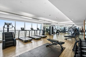 A gym with treadmills, weight machines, and a large window overlooking a cityscape.