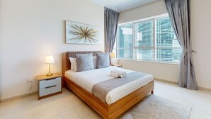 A modern bedroom with a large bed, a nightstand, a wall-mounted lamp, and a window with curtains. - Elegant 1 Bed l City Views l JLT (Jumeirah Lake Towers)