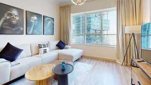 A modern living room with a white sofa, a round wooden coffee table, and a black side table with a blue decorative item. - Elegant 1 Bed l City Views l JLT (Jumeirah Lake Towers)