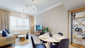 A modern living room with a sofa, a dining table set for four, and a television. - Elegant 1 Bed l City Views l JLT (Jumeirah Lake Towers)