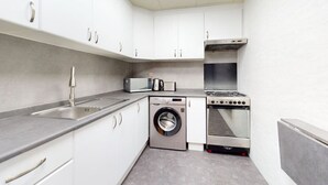 A compact kitchen with white cabinets, a stainless steel sink, a microwave, a washing machine, and a stove. - Elegant 1 Bed l City Views l JLT (Jumeirah Lake Towers)
