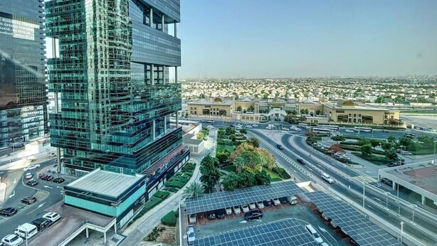 A modern high-rise building with a glass facade, surrounded by a well-maintained urban area with roads and greenery. - Elegant 1 Bed l City Views l JLT (Jumeirah Lake Towers)