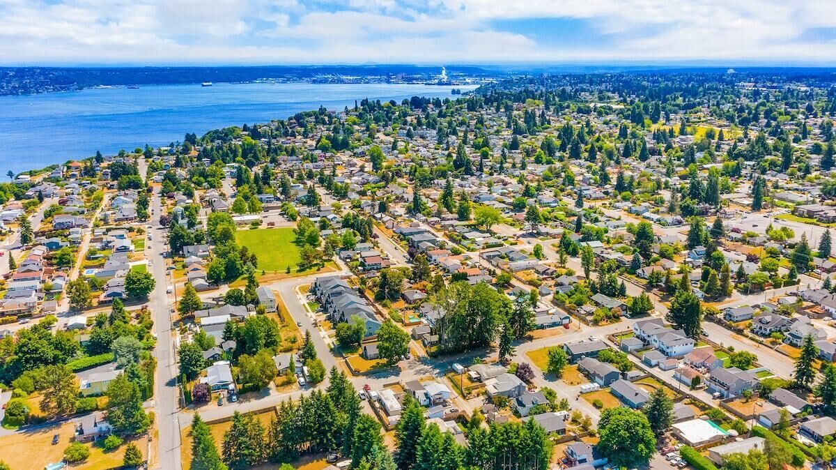 An aerial view of a residential area with houses, roads, and a body of water in the background.