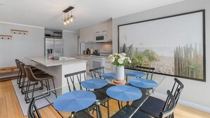 A modern kitchen with a central island, bar stools, and a dining area with blue chairs.