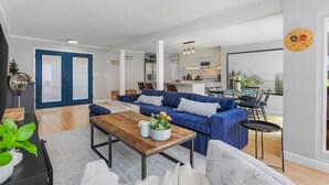 A modern living room with a blue sofa, wooden coffee table, and a dining area with a small table and chairs.