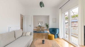A modern living room with a sofa, a round coffee table, a blue armchair, and a dining area in the background. - Flawless 1BR Apartment in Athens (Menemeni)