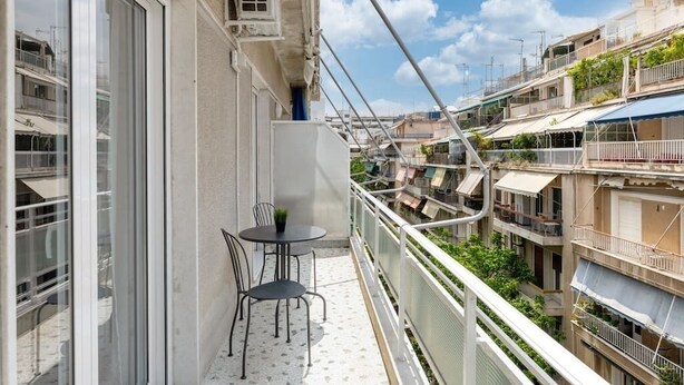 A balcony with a small table and chairs, overlooking a densely packed urban area with multiple buildings and balconies. - Flawless 1BR Apartment in Athens (Menemeni)