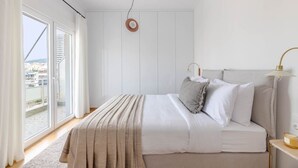 A bedroom with a bed, a bedside lamp, and a view of the outside. - Flawless 1BR Apartment in Athens (Menemeni)