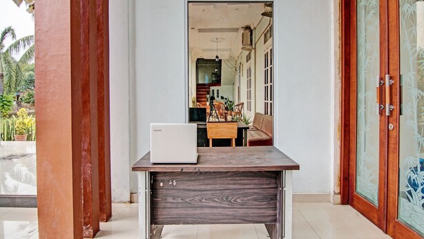 A room with a wooden desk, a laptop, and a view of a dining area with a sofa and chairs.