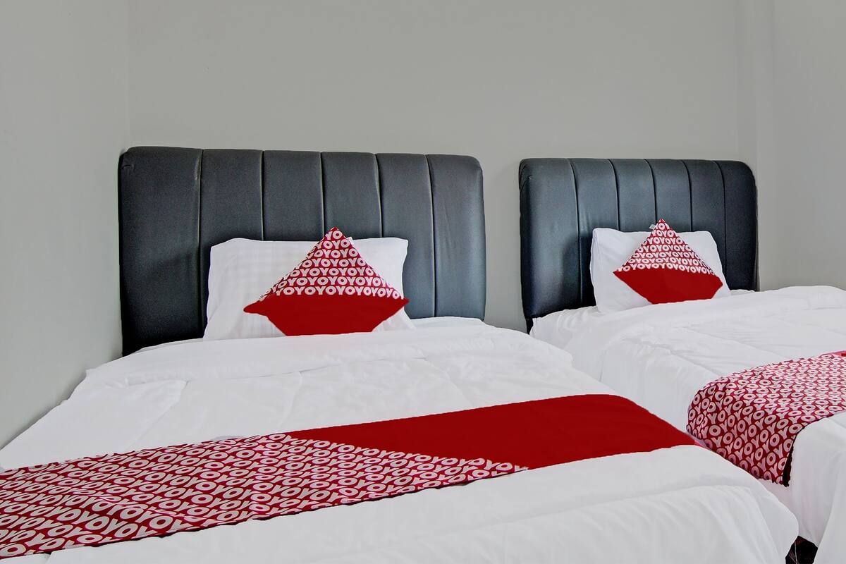 Ein Hotelzimmer mit zwei Betten, jeweils mit dunklem Kopfteil, weißer Bettwäsche und roten Kissen mit Muster.
