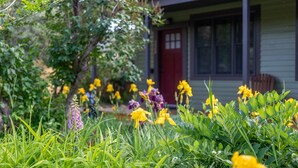 A garden with yellow and purple flowers in front of a house with a red door and windows. - The Garden House in Livingston (Livingston)