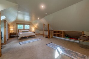 Ein geräumiges Schlafzimmer im Dachgeschoss mit einem großen Bett, einem Schlafplatz in einem hölzernen Hochbett und einem Fenster, das natürliches Licht hereinlässt.