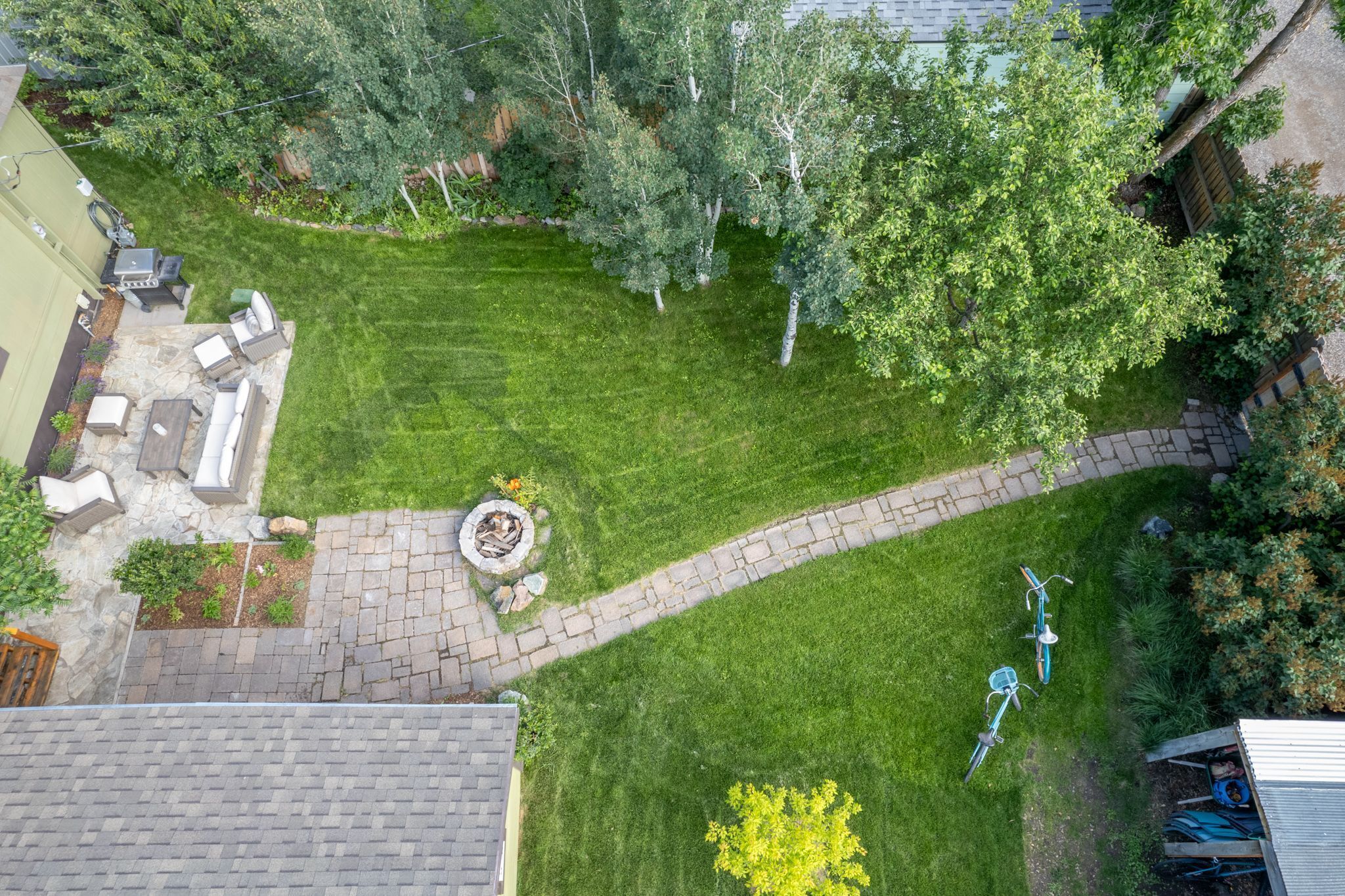 A well-maintained backyard with a stone patio, a fire pit, and a bicycle path.