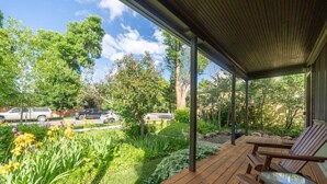 A covered outdoor area with wooden deck seating and a view of a garden with various plants and flowers. - The Garden House in Livingston (Livingston)