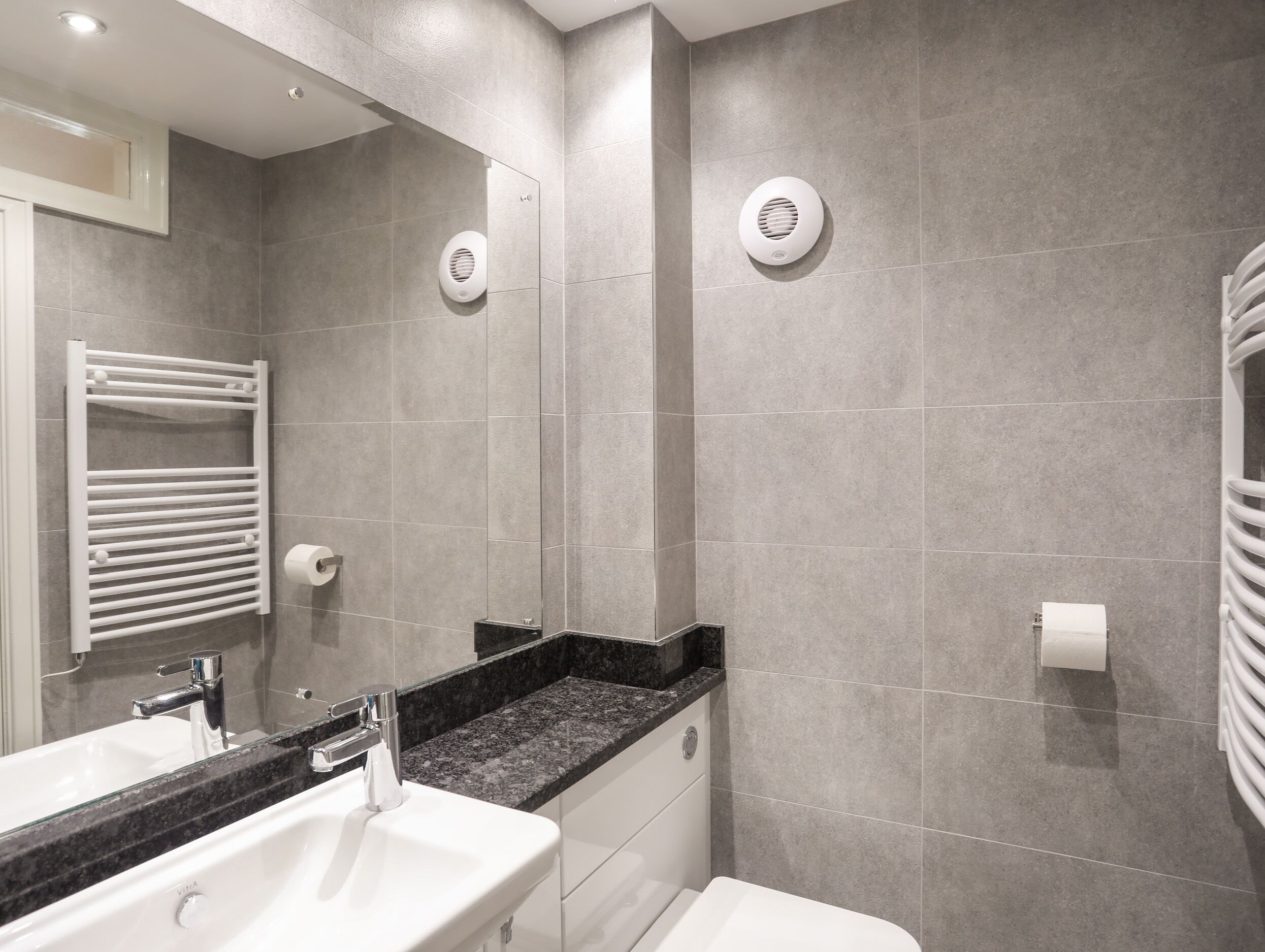 A modern bathroom with a large mirror, a white sink, a black countertop, and a white toilet.