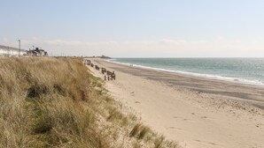 A beach with a wooden walkway, a dune, and buildings in the background. - 7 Min Y Traeth (Pwllheli)