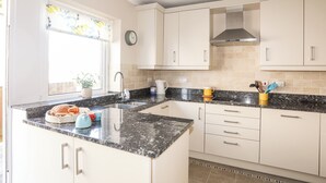 A kitchen with white cabinets, a granite countertop, a stainless steel sink, and a clock on the wall. - 7 Min Y Traeth (Pwllheli)