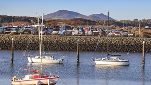 A marina with boats docked, a rocky breakwater, and a mountain in the background. - 7 Min Y Traeth (Pwllheli)