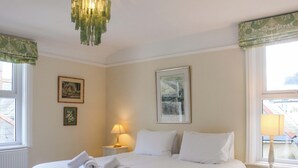 A neatly made bed with white linens and rolled towels, a bedside table with a lamp, and framed artwork on the walls. - 29b Lower Street (Dartmouth)