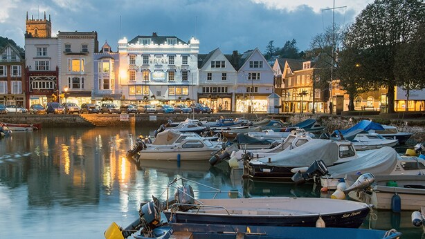 A marina with several boats docked, a castle hotel in the background, and a row of shops along the waterfront. - 29b Lower Street (Dartmouth)