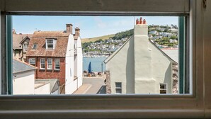 A view through a window of a coastal town with buildings, a marina, and hills in the background. - 29b Lower Street (Dartmouth)