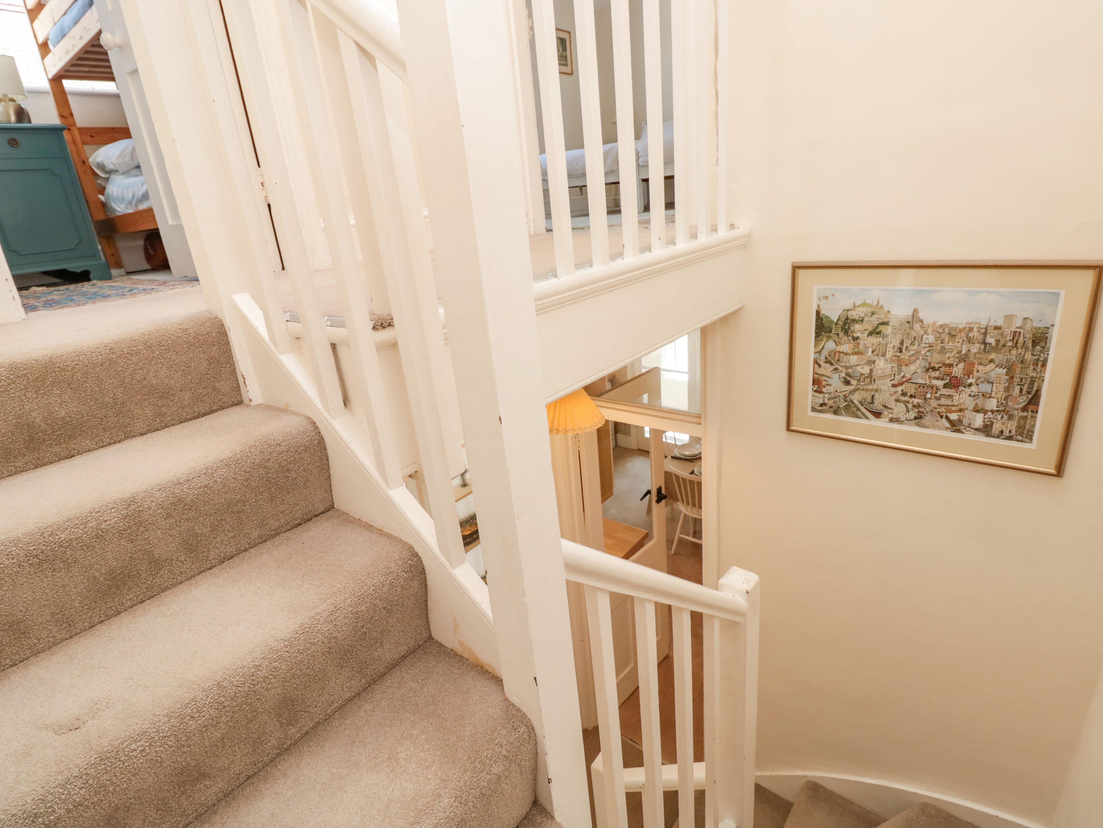 A staircase with beige carpeted steps and white railings, leading to a lower level. A framed cityscape painting is visible on the wall.