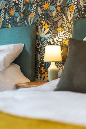 A neatly made bed with pillows, a bedside table with a lamp, and a floral wallpaper pattern. - Quiet Peaceful Location (Bristol)