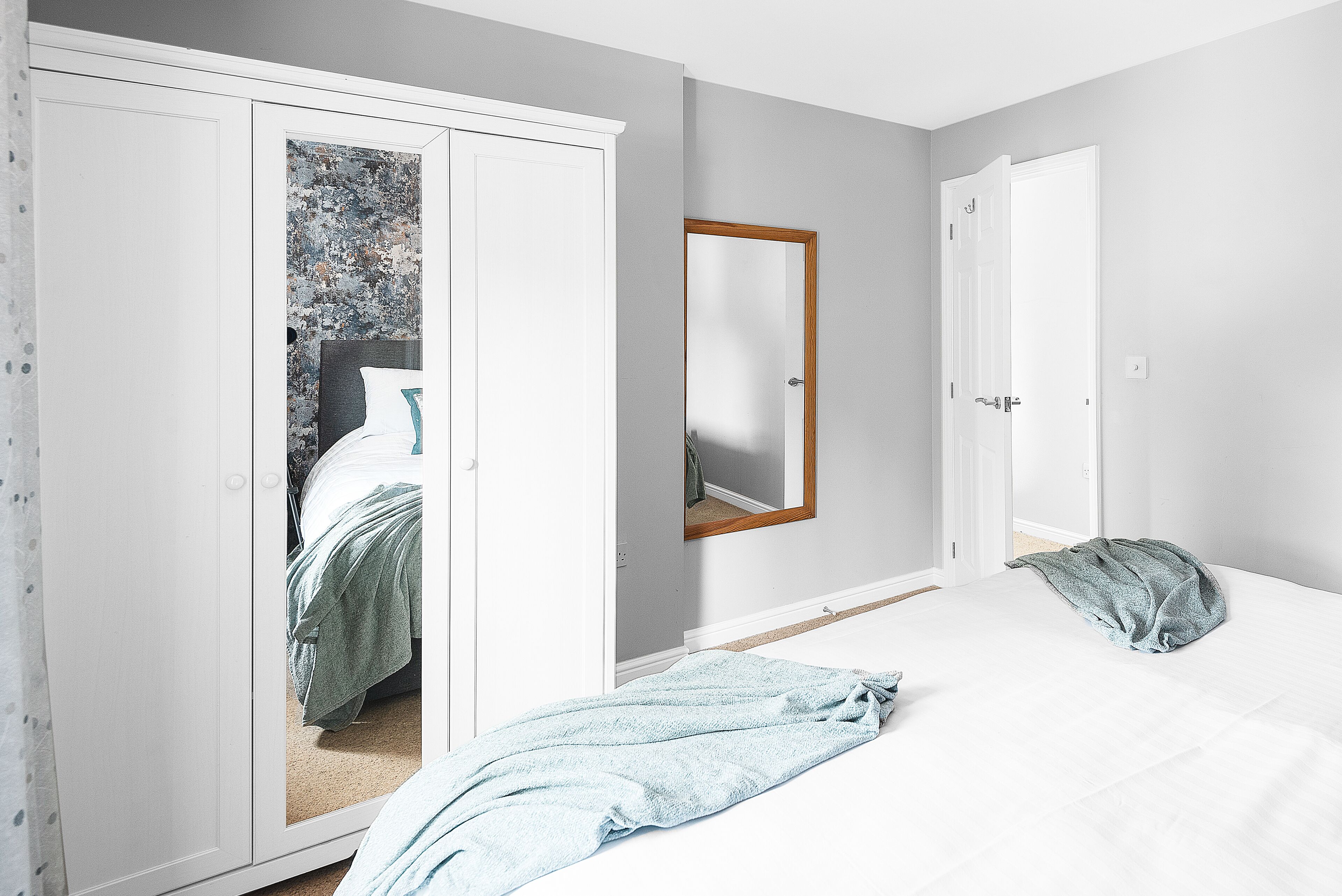 Een slaapkamer met een bed, een kledingkast en een spiegel aan de muur.