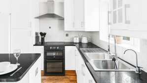 A modern kitchen with white cabinets, a black countertop, stainless steel appliances, and a wooden floor. - Quiet Peaceful Location (Bristol)