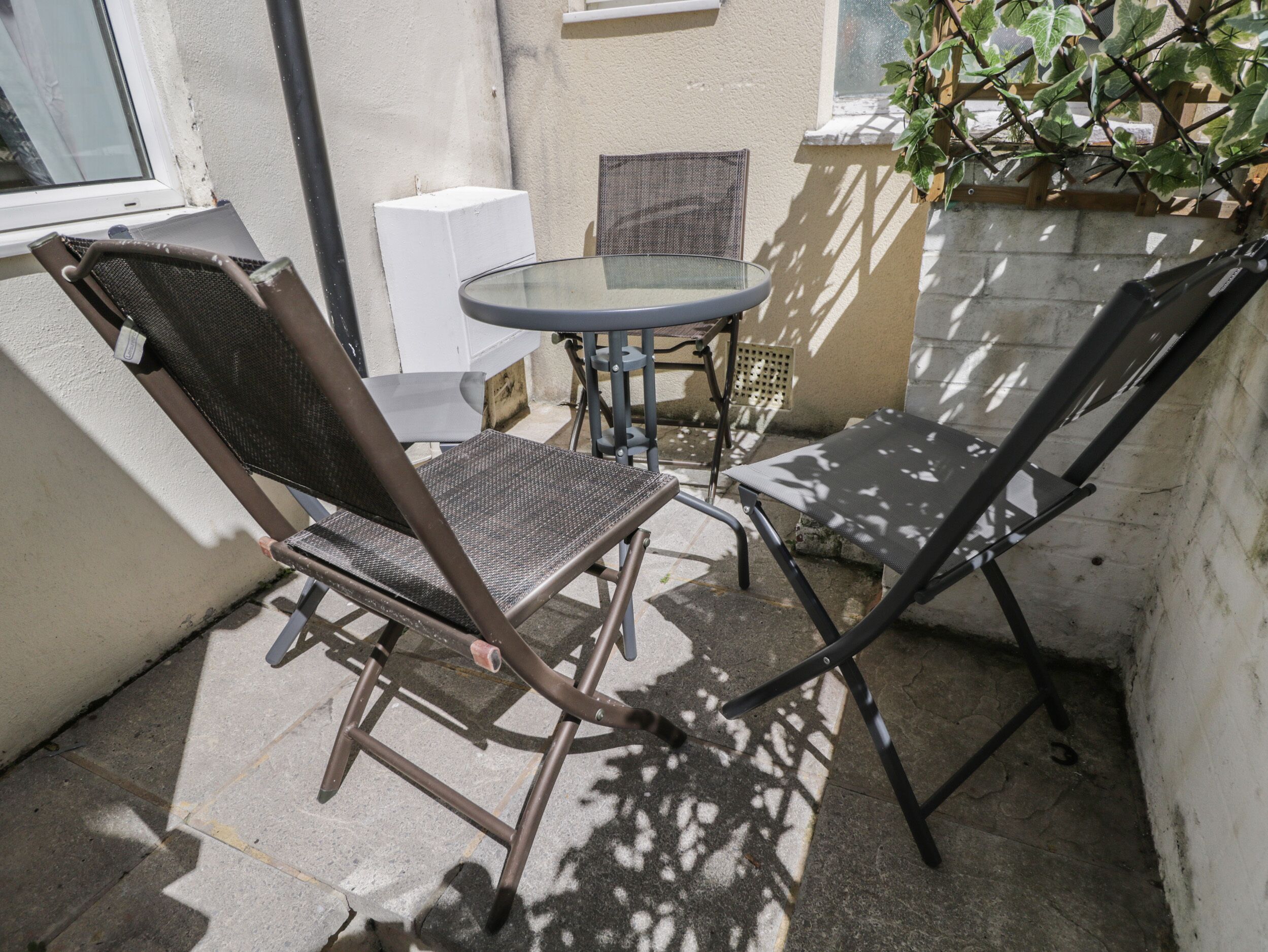 Pequeño patio con una mesa redonda de vidrio y dos sillas de metal.