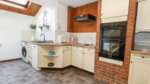 A kitchen with a washing machine, a stove, and a brick wall.