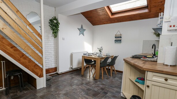 A compact kitchen with a dining area, wooden staircase, and a skylight.